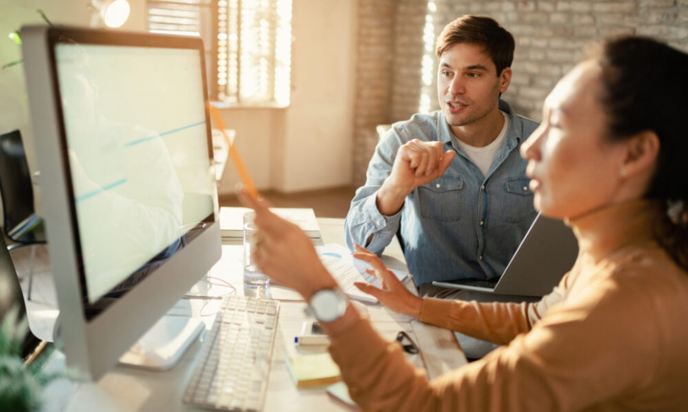 Freelance workers communicating while working together on desktop PC in the office.