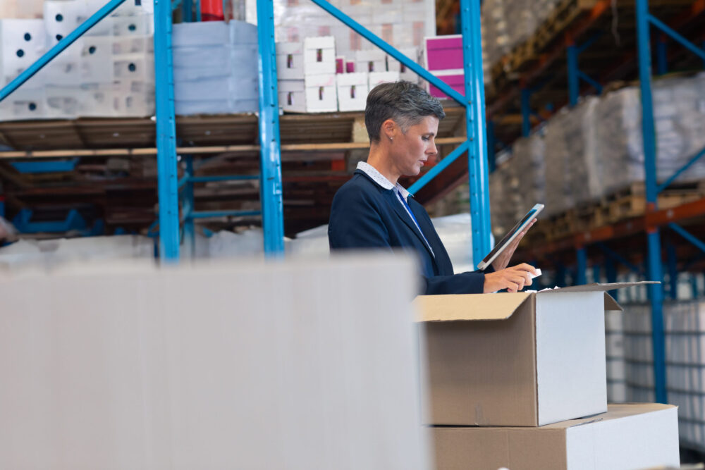 Warehouse manager using a tablet to inspect inventory, representing the use of warehouse management system software in a modern distribution facility.