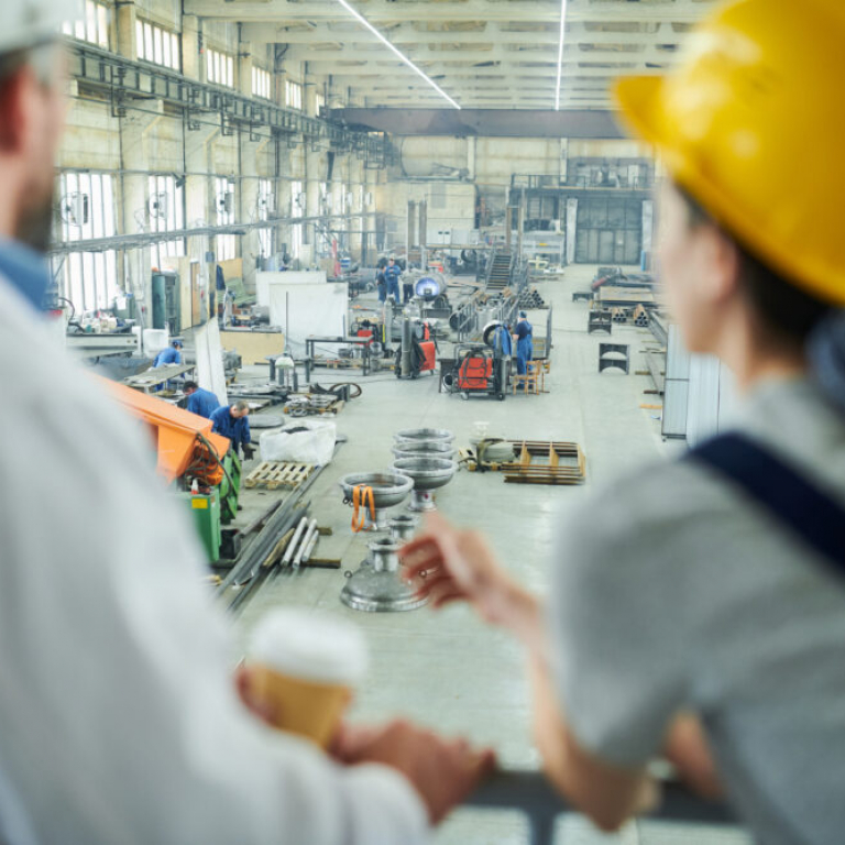 Engineers overlooking a busy factory floor with workers and machinery, highlighting the role of manufacturing software systems in managing production operations.