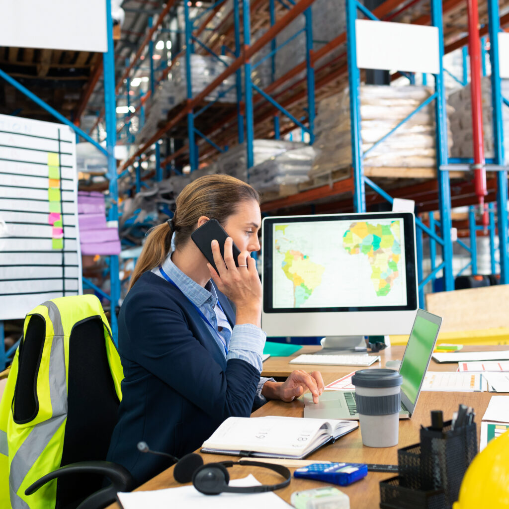 Businesswoman in warehouse talking on phone using NetSuite warehouse management system software to manage inventory
