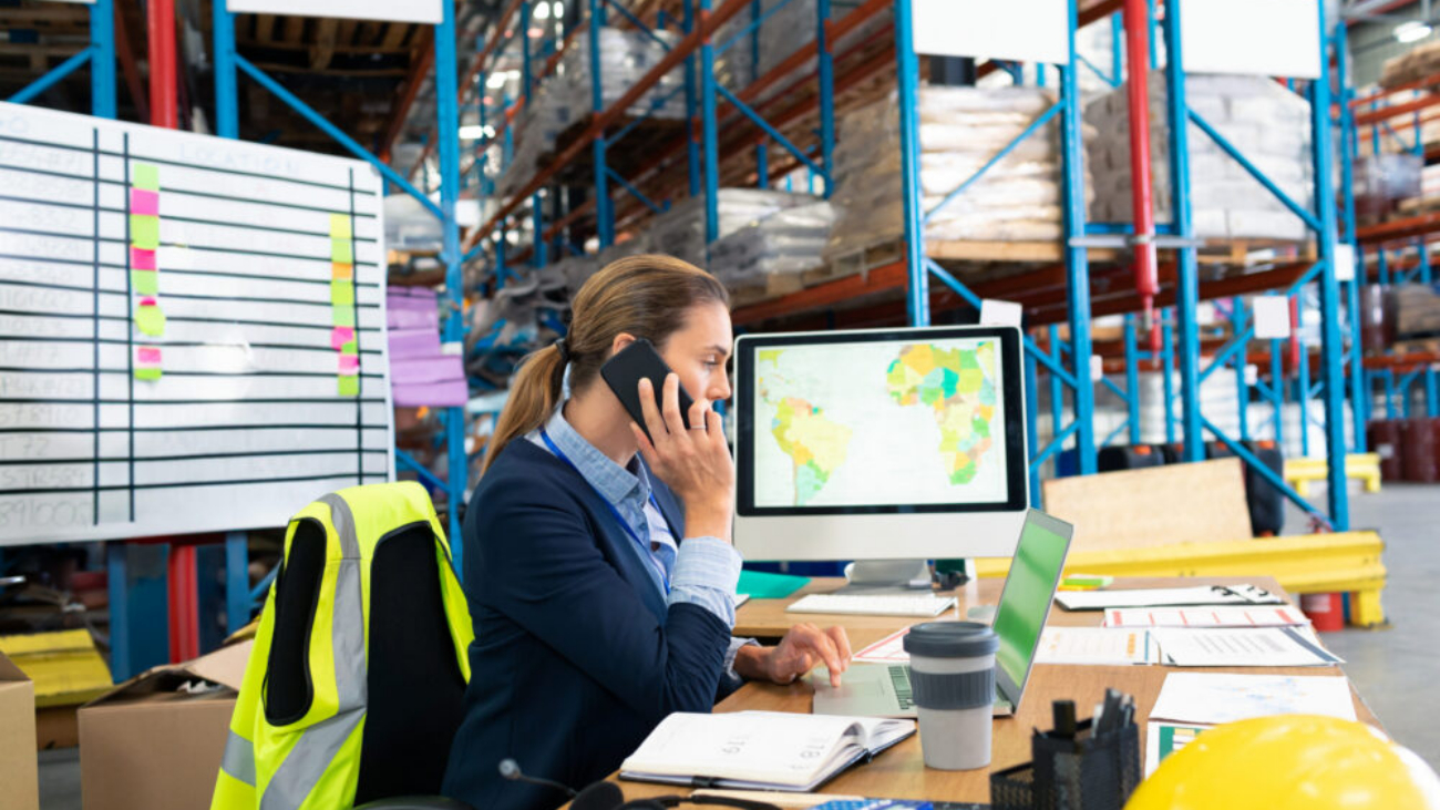 Businesswoman in warehouse talking on phone using NetSuite warehouse management system software to manage inventory