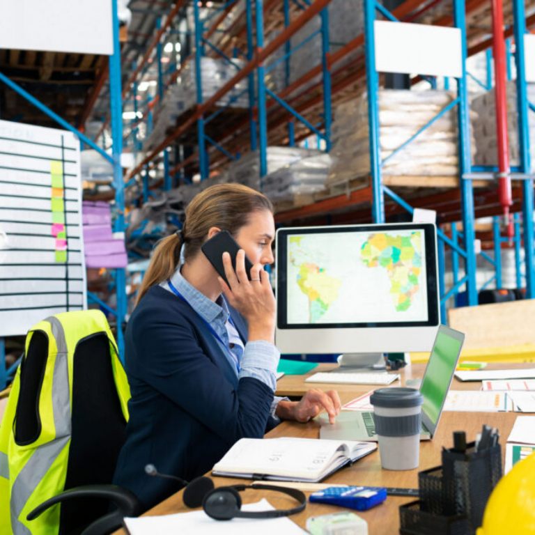 Businesswoman in warehouse talking on phone using NetSuite warehouse management system software to manage inventory