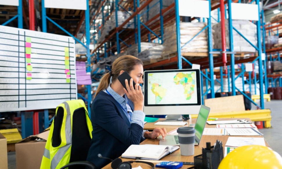 Businesswoman in warehouse talking on phone using NetSuite warehouse management system software to manage inventory