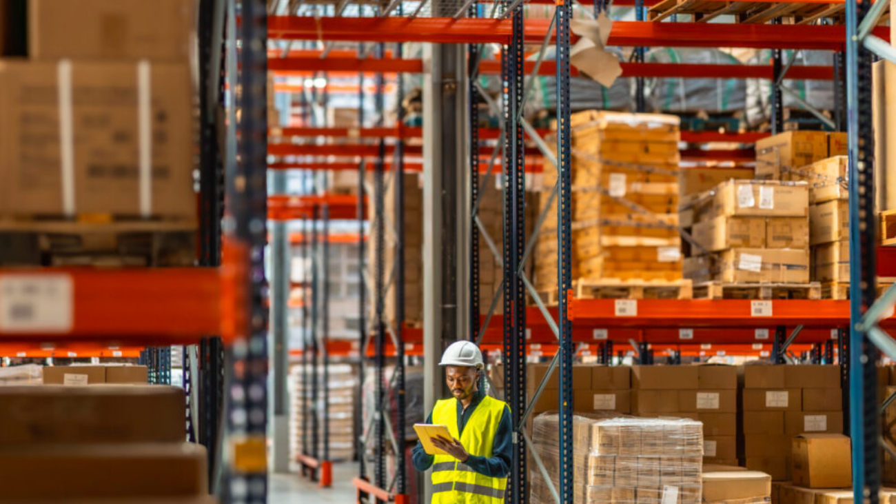 Man working in a warehouse using a digital tablet with Manufacturing ERP and Warehouse Management System Software to manage inventory and supply chain operations.