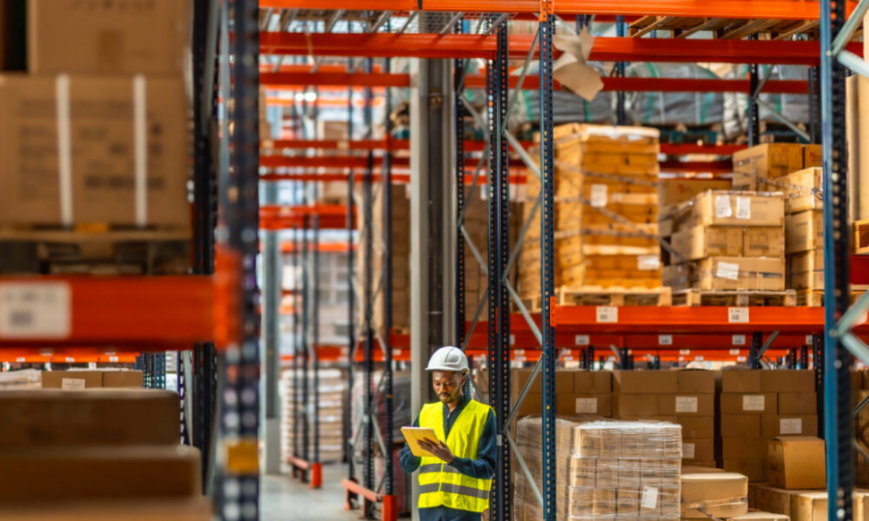 Man working in a warehouse using a digital tablet with Manufacturing ERP and Warehouse Management System Software to manage inventory and supply chain operations.
